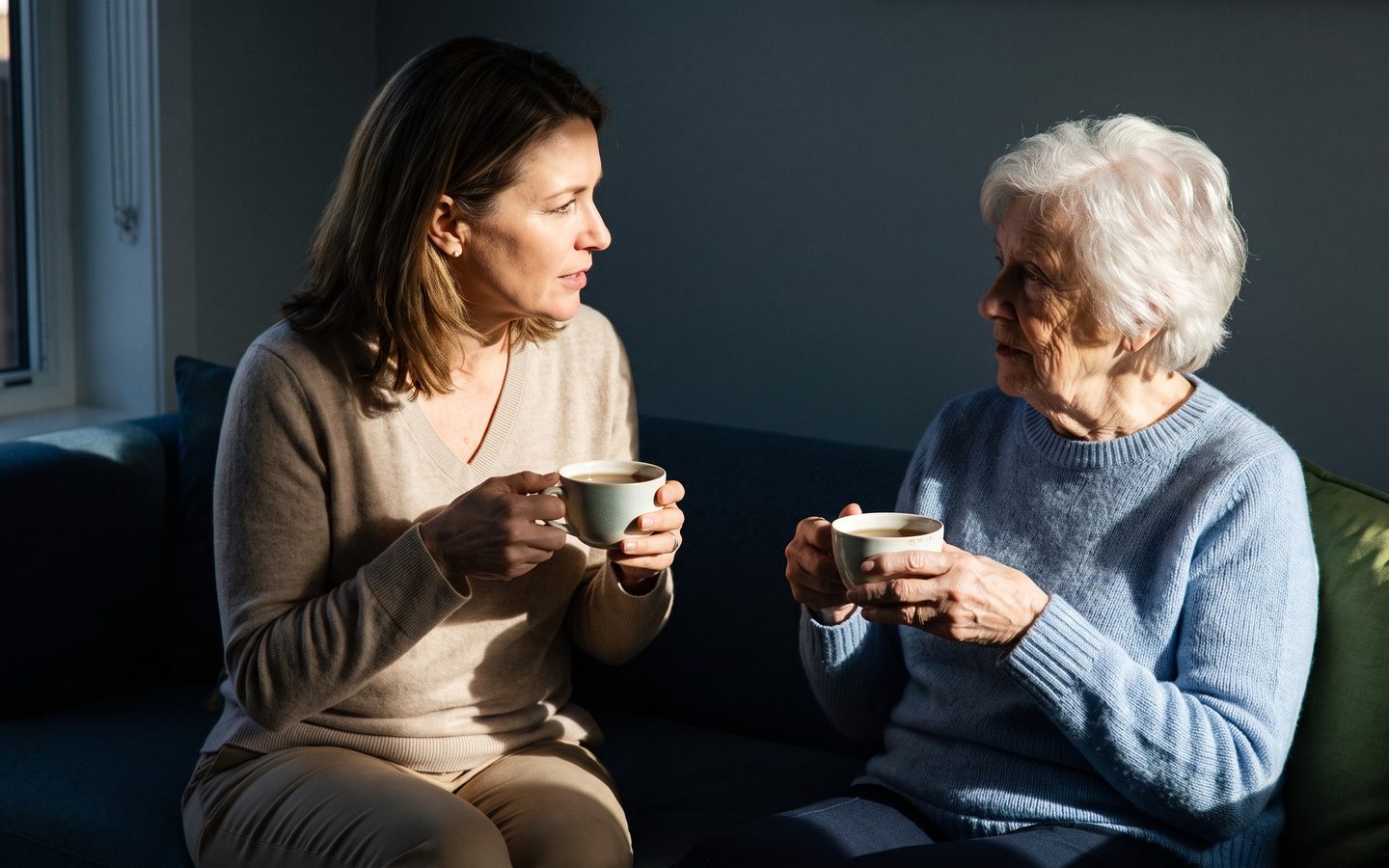 A caregiver and an older woman talking together over tea