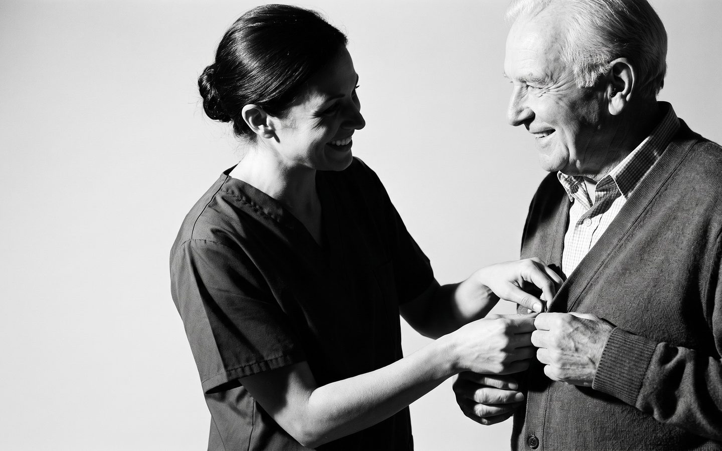 A caregiver helping a man button his cardigan