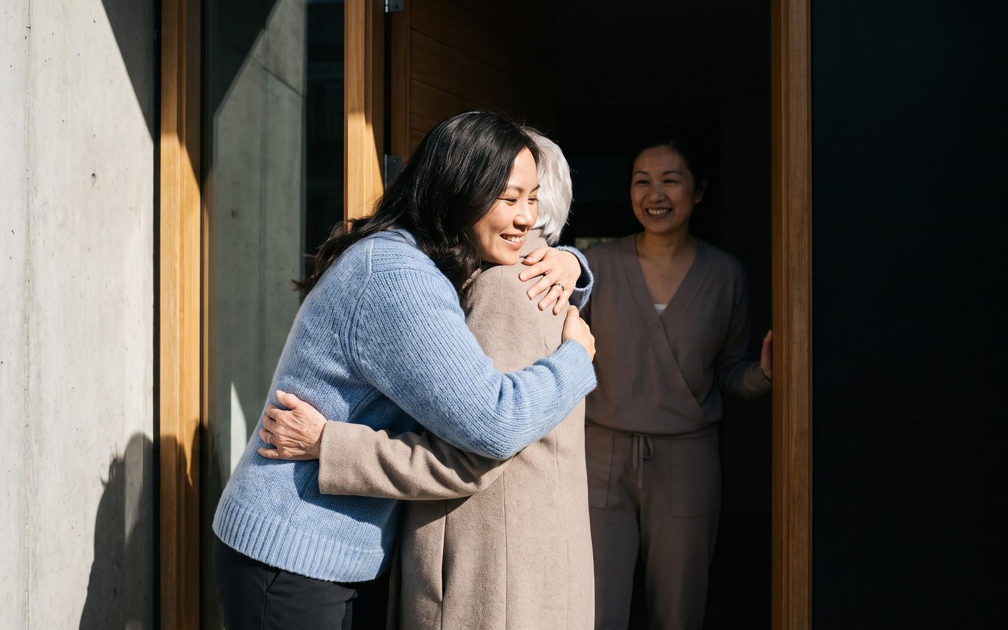 A daughter saying goodbye to her mother at the door as a caregiver arrives